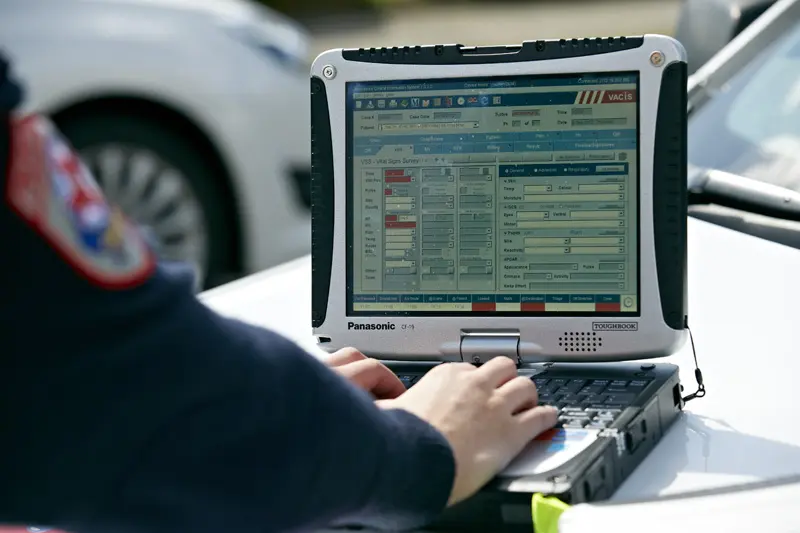 Medical professional EMT with toughbook laptop open on hood of car