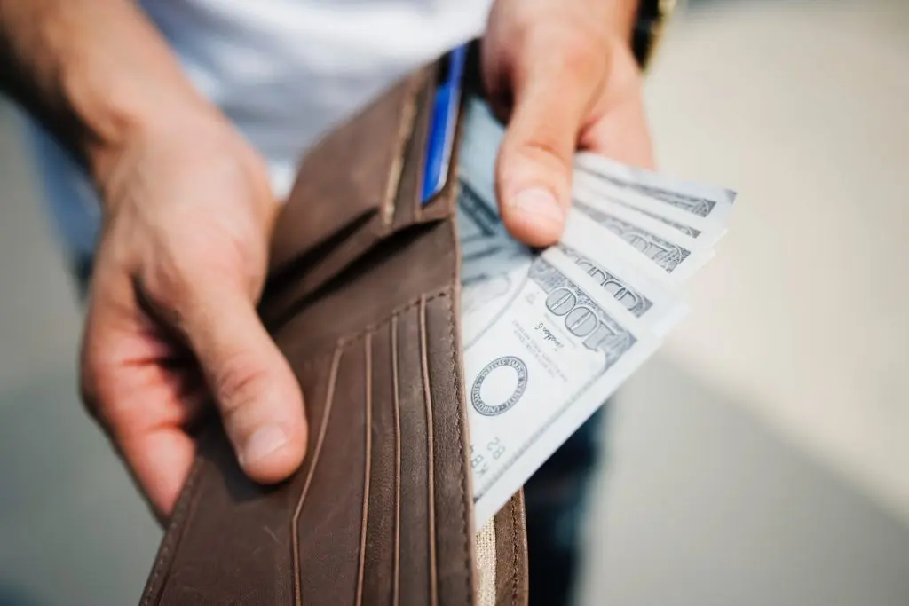 Two hands holding a wallet with 100 dollar bills
